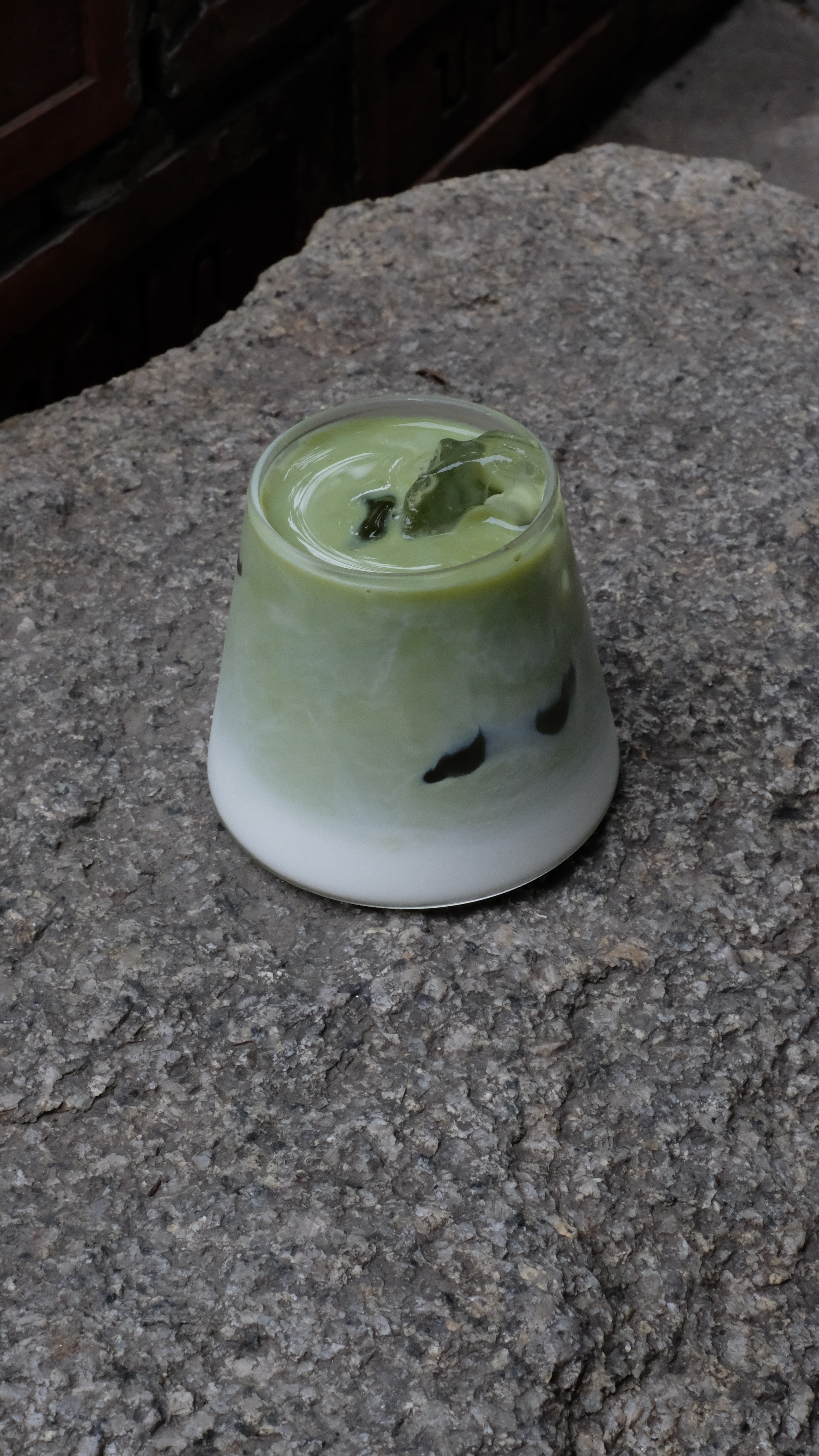 A creamy green and white iced beverage on a gray concrete countertop